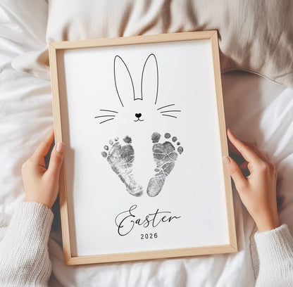 Framed keepsake with bunny design and baby footprints, held by hands on a soft surface.
