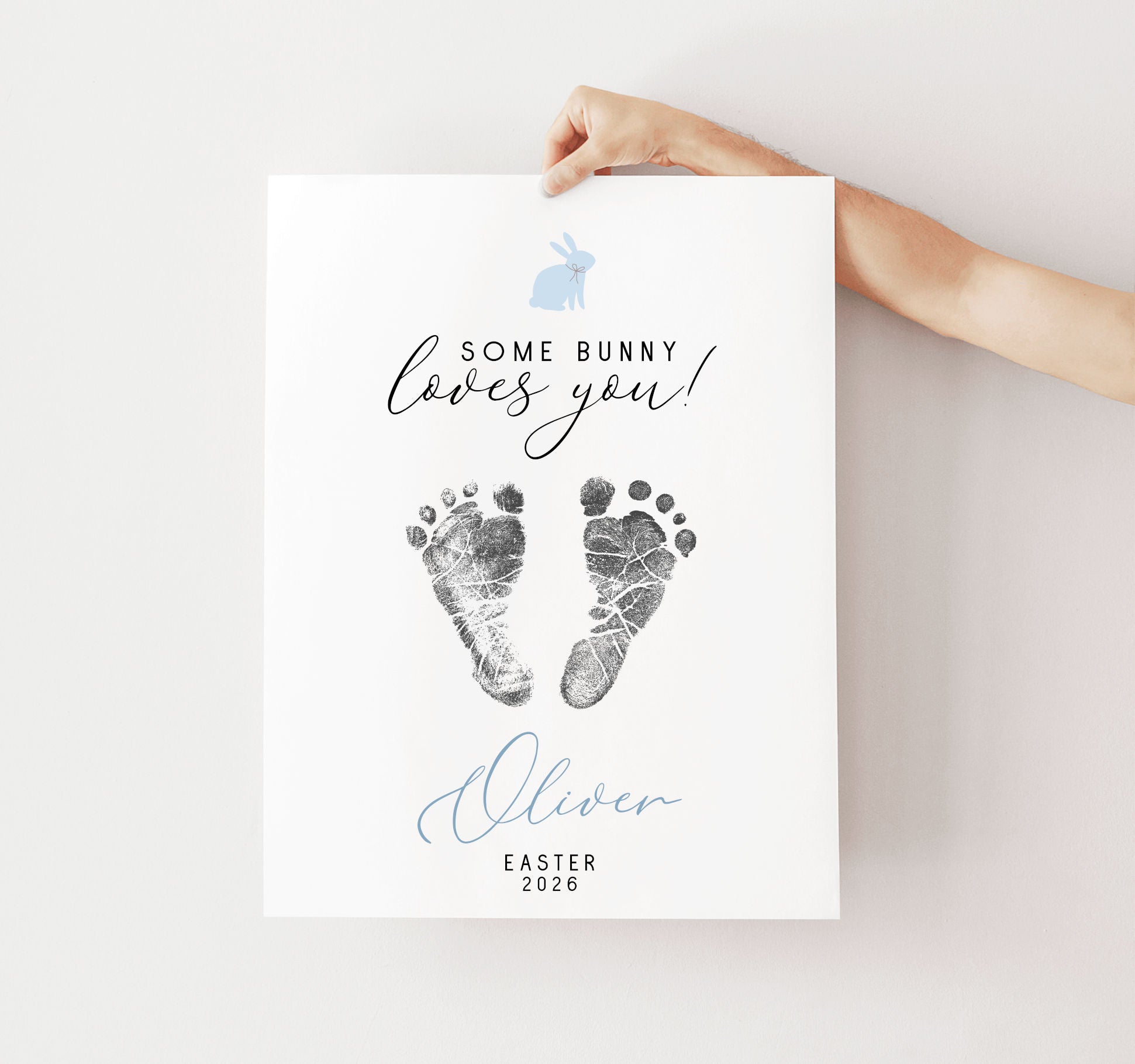Hand holding a keepsake with baby footprints and text 'Some Bunny Loves You' on a light background