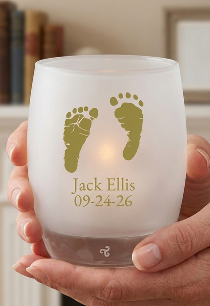 Frosted glass candle holder with gold footprints and text held by a hand.